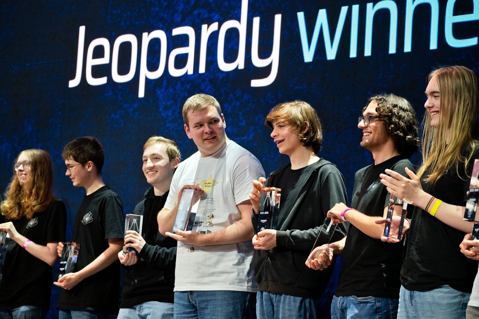Members of the German team laughing with glass trophies in front of the screen reading “Jeopardy winner”.