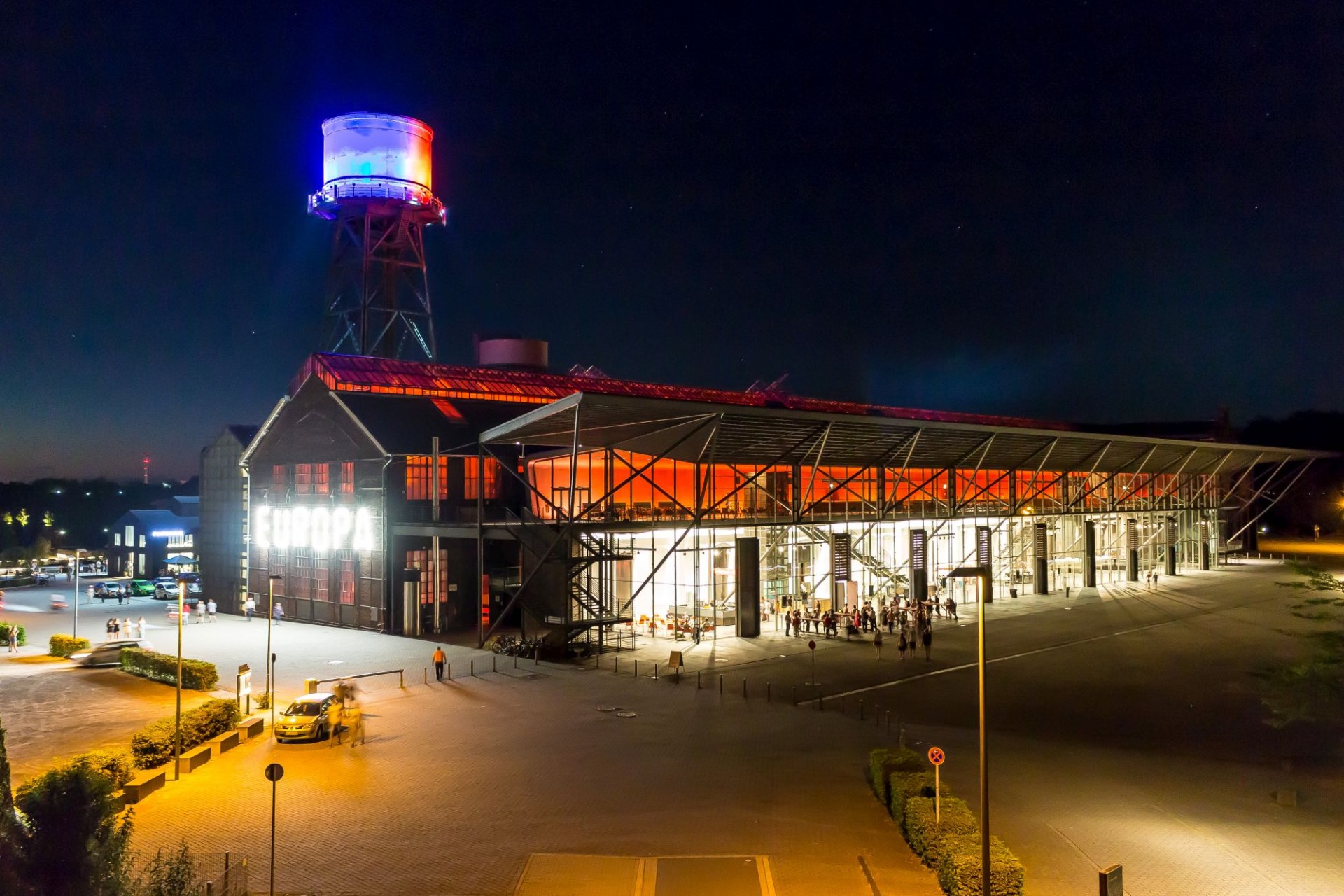 Jahrhunderthalle Bochum at night, with its illuminated glass entrance and colourful water tower